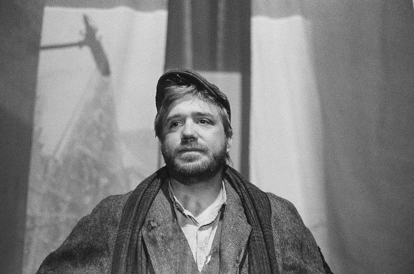 Toby Veck, in flat cap and heavy wool, looking up toward the bell tower.