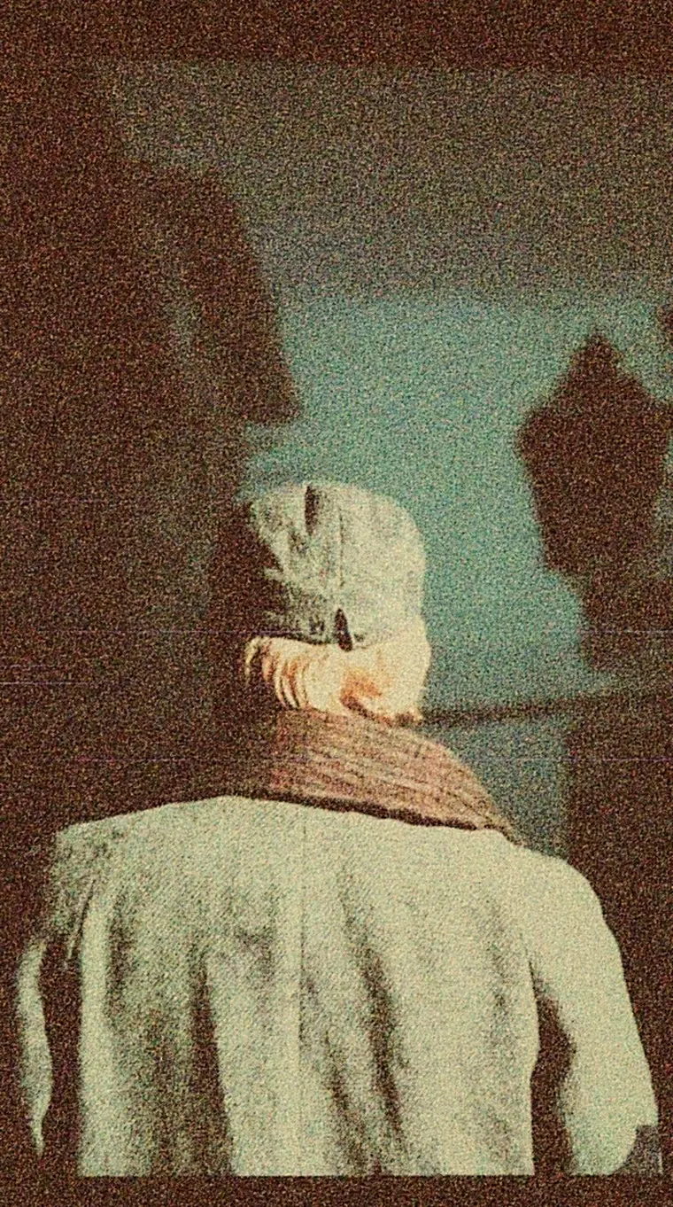 Meg, seen from behind in a pale headscarf, facing a cold doorway.